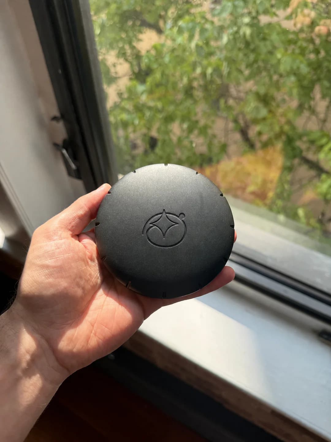 Matte black round Oneira package with an embossed logo, held in one hand by a window.
